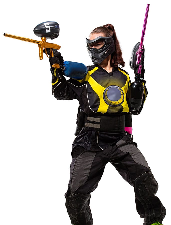 A person wearing protective gear and a mask holds two paintball markers, one gold and one pink, ready for action—perfect for hen parties. The outfit features a yellow and black jersey with padded pants and gloves.