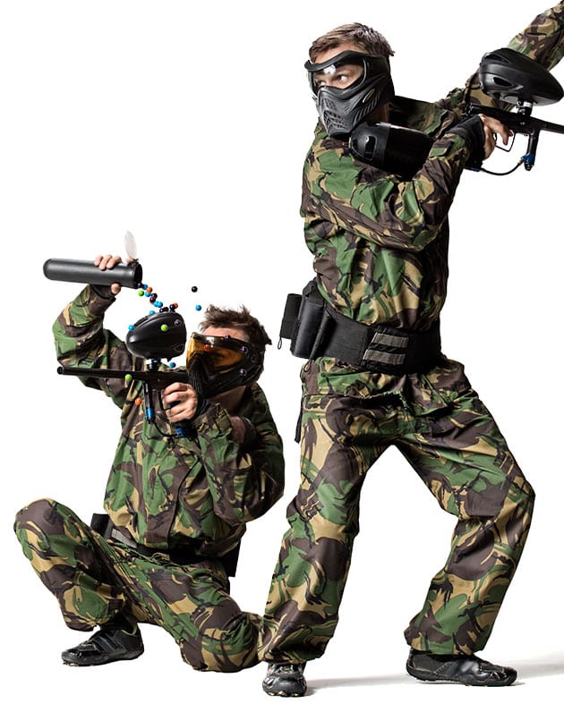 Two people in camouflage outfits and protective masks pose with paintball guns; perfect for a team building activity. One kneels to load paintballs while the other stands ready to shoot, both in black shoes against a white background.