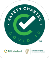 Green circular badge with a white checkmark and text reading SAFETY CHARTER COVID-19. Logos for Fáilte Ireland and the Government of Ireland are at the bottom.