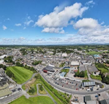 Aerial view of a small town with scattered buildings, green fields, winding roads, and a partly cloudy blue sky, offering useful information for those interested in local geography and landscape planning.