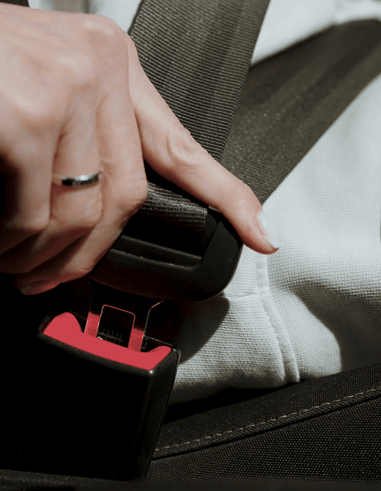 A person wearing a silver ring fastens a black seatbelt into its buckle while sitting in a car seat, demonstrating the importance of safety for young drivers.