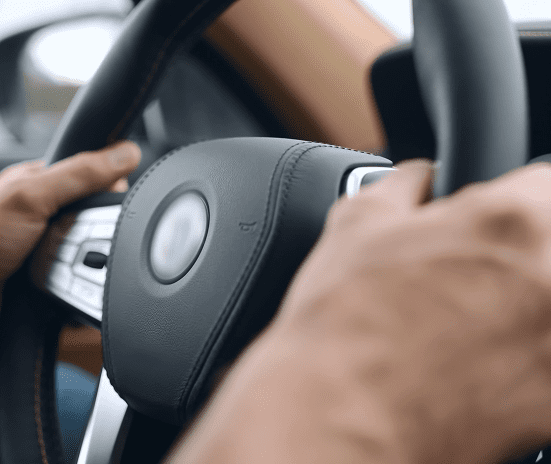 Close-up of a person’s hands gripping a black leather steering wheel inside a car, with one hand about to press the horn in the center.